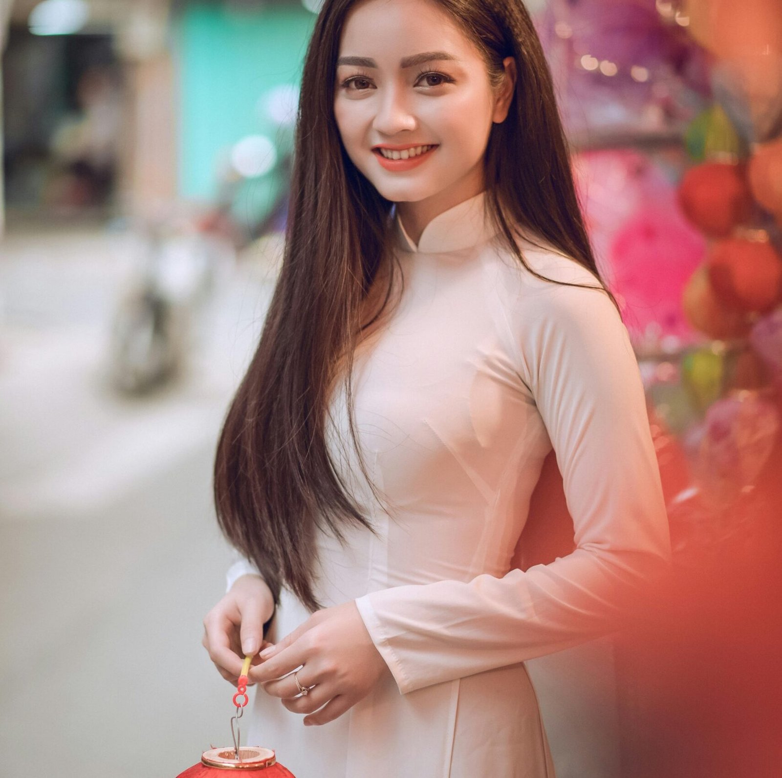 Portrait of a smiling young woman holding a lantern in a vibrant street setting.