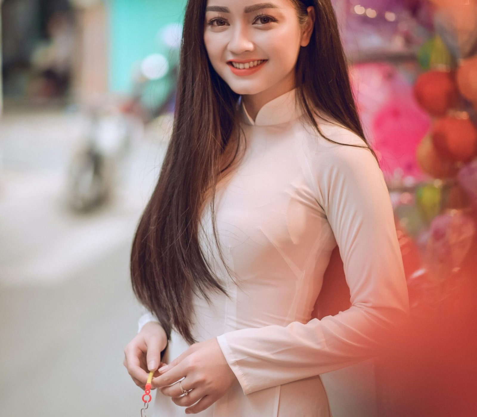 Portrait of a smiling young woman holding a lantern in a vibrant street setting.